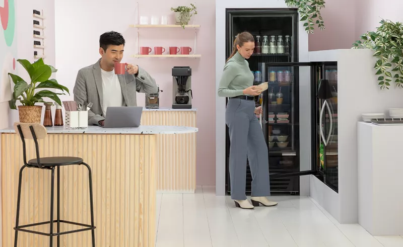 Man drinking coffee and women looking in fridge cabinet